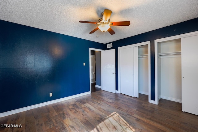 unfurnished bedroom featuring dark wood-type flooring, ceiling fan, a textured ceiling, and two closets