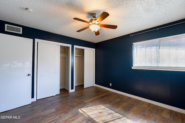 unfurnished bedroom with dark wood-type flooring, ceiling fan, multiple closets, and a textured ceiling