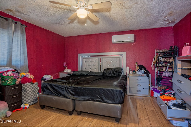 bedroom featuring light wood finished floors, a ceiling fan, a textured ceiling, and a wall mounted AC