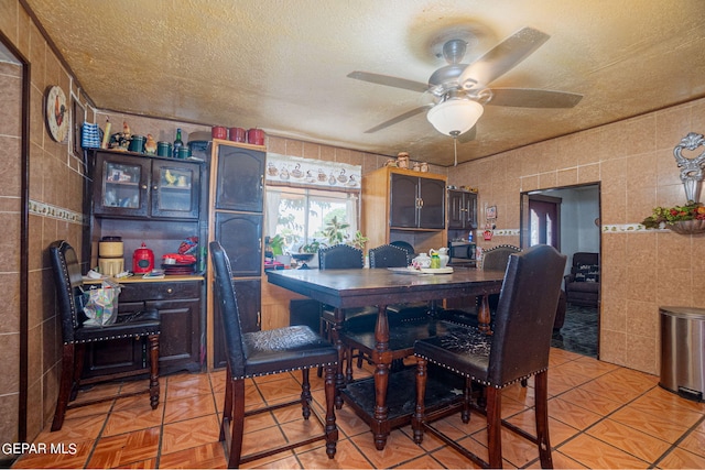 dining room featuring ceiling fan, a textured ceiling, and tile walls