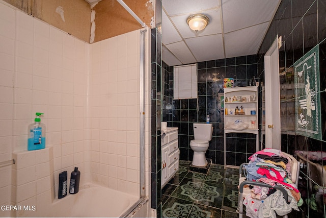 full bath with tile walls, a paneled ceiling, shower / bath combination, toilet, and tile patterned flooring