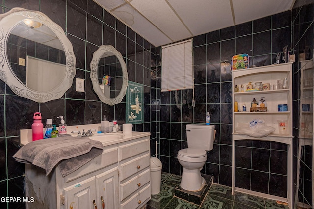 bathroom with toilet, vanity, and tile walls