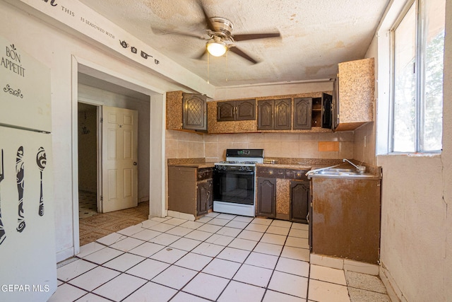 kitchen with white gas stove, backsplash, a ceiling fan, a sink, and a textured ceiling