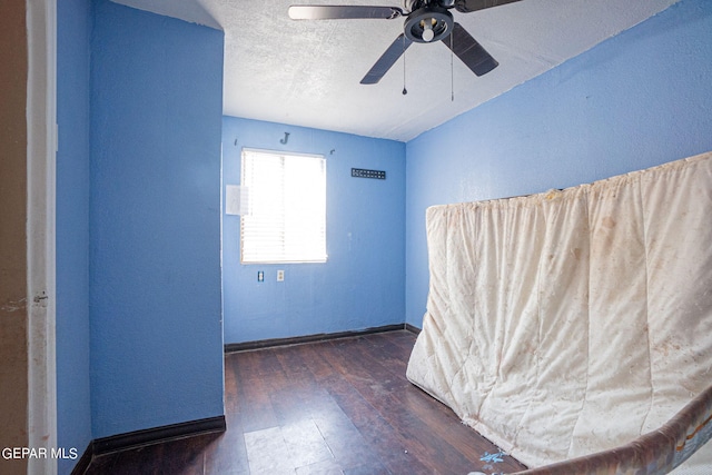 unfurnished room featuring dark wood-style flooring, a textured wall, ceiling fan, a textured ceiling, and baseboards