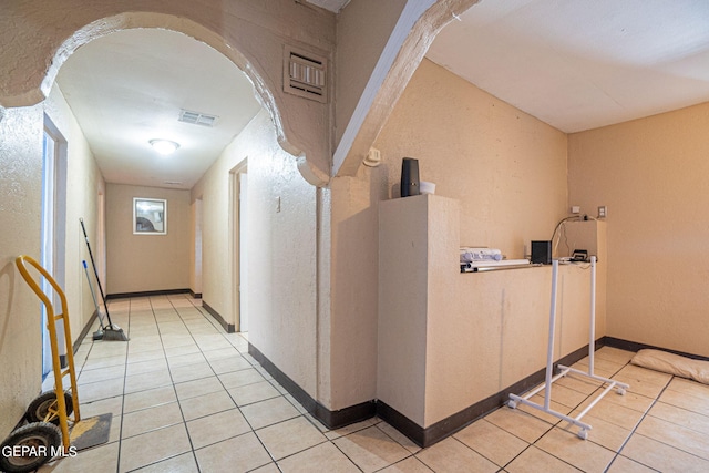 corridor featuring light tile patterned floors, arched walkways, visible vents, and baseboards