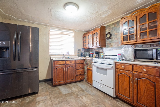 kitchen featuring a textured ceiling, stainless steel appliances, light countertops, brown cabinetry, and glass insert cabinets