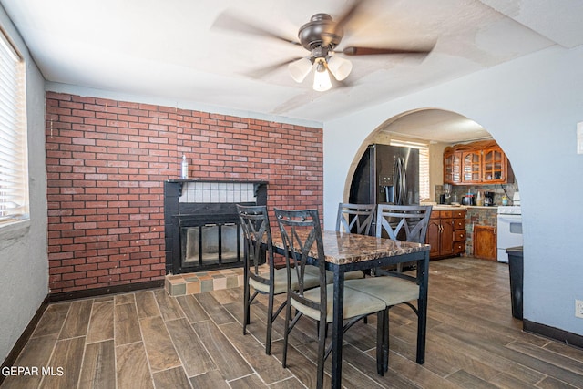 dining space with baseboards, a fireplace, arched walkways, and wood finish floors