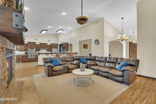 living room featuring a fireplace, light hardwood / wood-style floors, a notable chandelier, and high vaulted ceiling