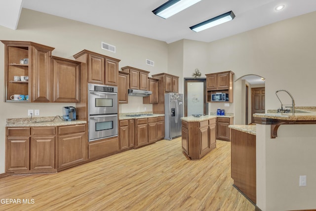 kitchen featuring a high ceiling, a kitchen island, stainless steel appliances, light hardwood / wood-style floors, and light stone countertops