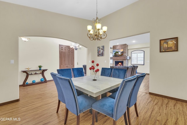 dining space with an inviting chandelier, brick wall, a fireplace, and light hardwood / wood-style floors