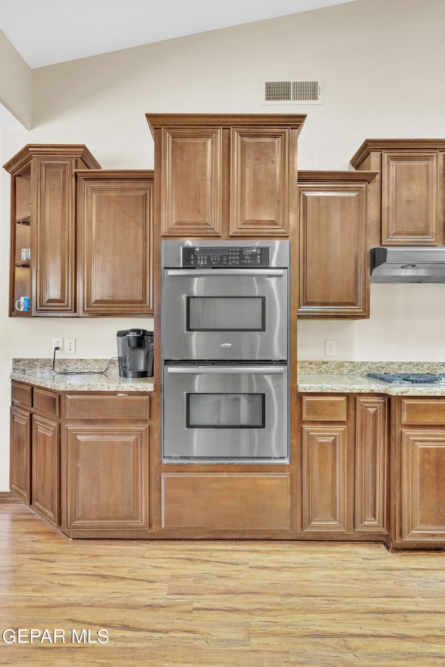 kitchen featuring appliances with stainless steel finishes, extractor fan, light hardwood / wood-style floors, light stone countertops, and lofted ceiling