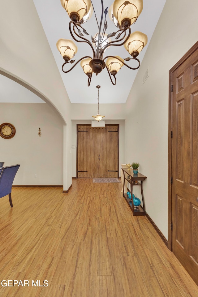 entrance foyer featuring vaulted ceiling, a notable chandelier, and light hardwood / wood-style floors