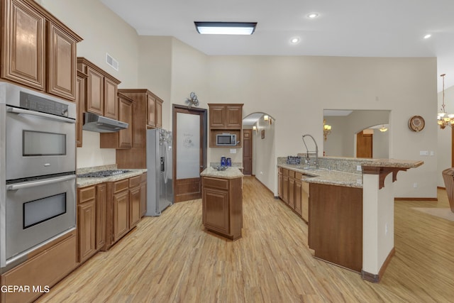 kitchen with appliances with stainless steel finishes, light stone counters, decorative light fixtures, light wood-type flooring, and a center island