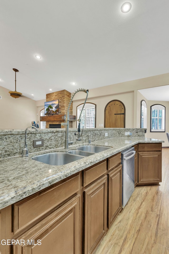 kitchen featuring sink, stainless steel dishwasher, light stone countertops, and light hardwood / wood-style flooring