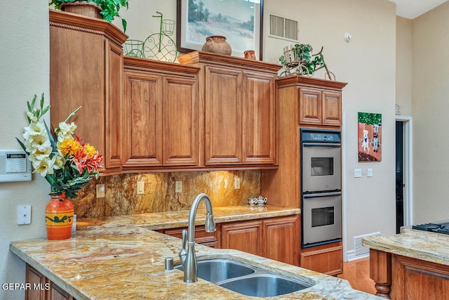 kitchen featuring light stone counters, sink, backsplash, and stainless steel double oven