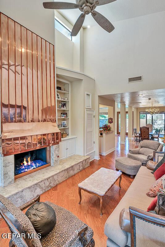 living room with ceiling fan, hardwood / wood-style floors, a towering ceiling, a high end fireplace, and built in shelves