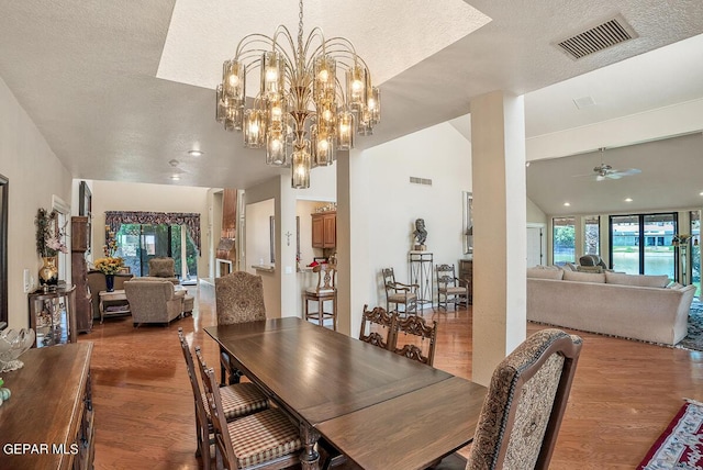 dining area with wood-type flooring, lofted ceiling, ceiling fan with notable chandelier, and a textured ceiling