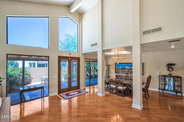 foyer with wood-type flooring, a towering ceiling, a chandelier, and french doors