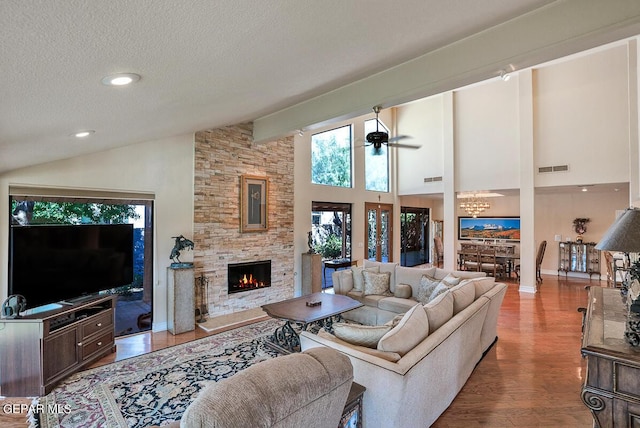 living room featuring a stone fireplace, high vaulted ceiling, a textured ceiling, light wood-type flooring, and ceiling fan