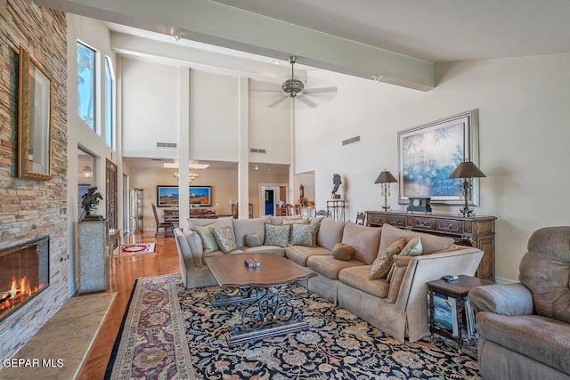 living room with a stone fireplace, high vaulted ceiling, beamed ceiling, ceiling fan, and light hardwood / wood-style floors