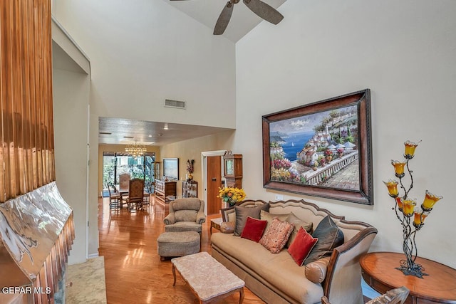 living room featuring a towering ceiling, ceiling fan with notable chandelier, and light hardwood / wood-style flooring