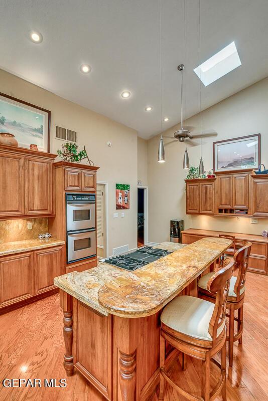 kitchen featuring appliances with stainless steel finishes, hanging light fixtures, a kitchen breakfast bar, light stone countertops, and a kitchen island