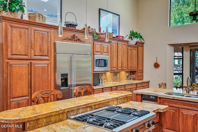 kitchen with sink, built in appliances, pendant lighting, decorative backsplash, and a high ceiling