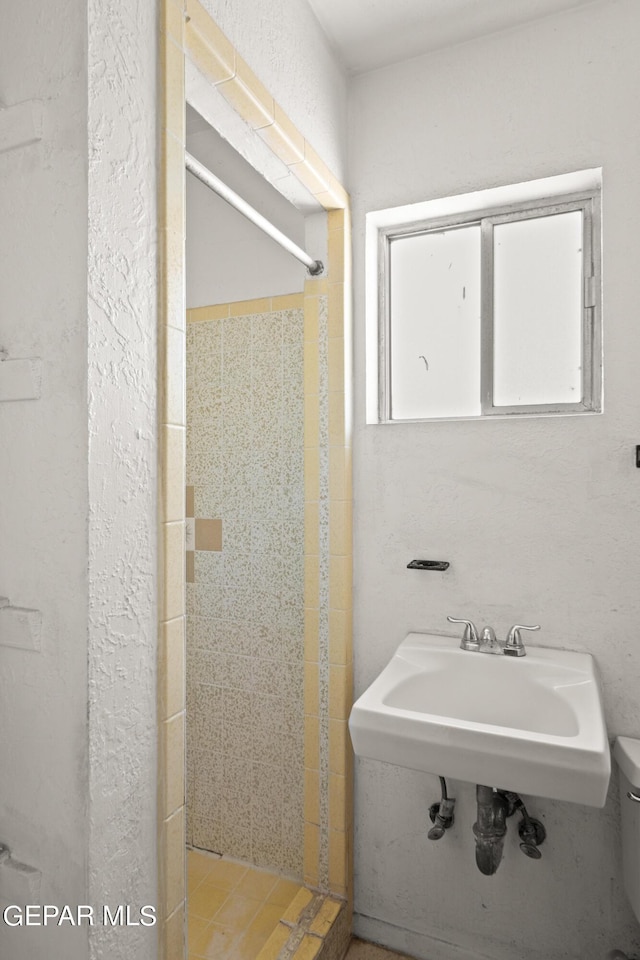 bathroom with tiled shower, sink, and toilet