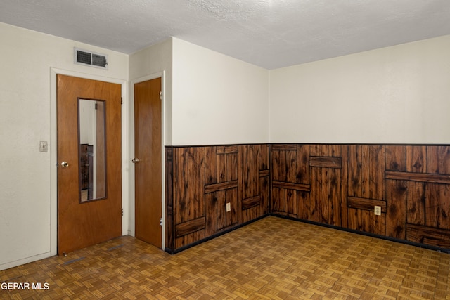 unfurnished room with parquet floors, a textured ceiling, and wood walls