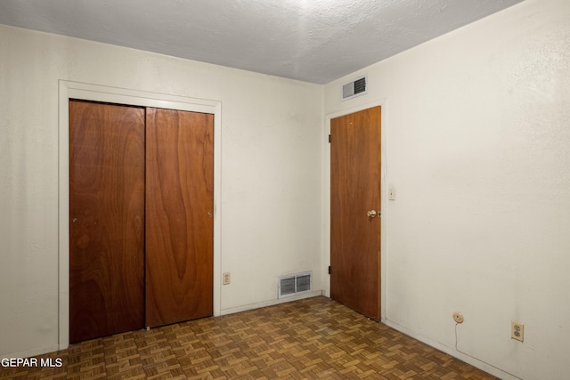 unfurnished bedroom with dark parquet floors, a closet, and a textured ceiling