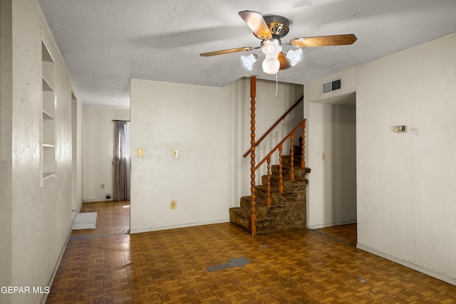 unfurnished room with built in shelves, ceiling fan, dark parquet flooring, and a textured ceiling