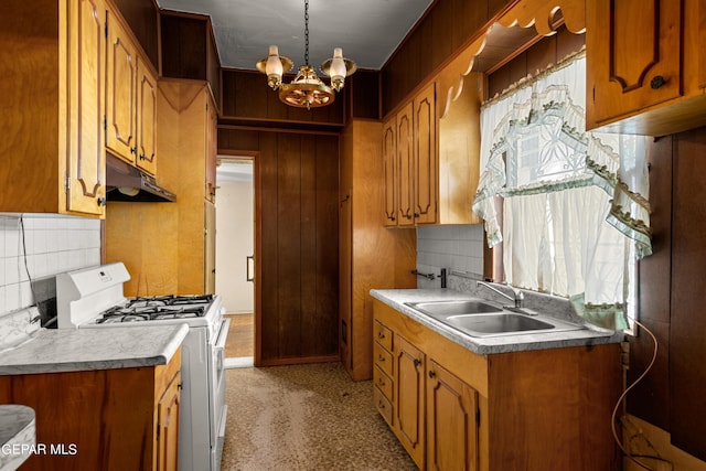 kitchen with sink, white range with gas stovetop, an inviting chandelier, wooden walls, and decorative backsplash