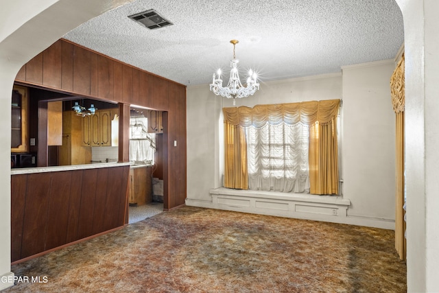 unfurnished dining area featuring dark carpet, ornamental molding, a chandelier, and a textured ceiling