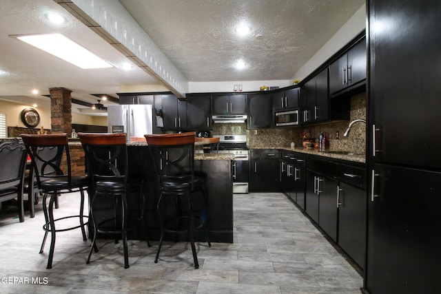 kitchen featuring a kitchen island, stainless steel appliances, light stone countertops, and sink