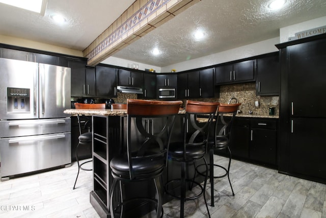 kitchen with a textured ceiling, appliances with stainless steel finishes, a breakfast bar area, and a center island