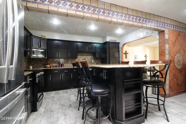 kitchen featuring appliances with stainless steel finishes, tasteful backsplash, a textured ceiling, and a breakfast bar area