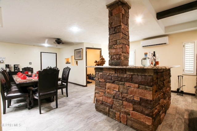 dining room with beam ceiling, light wood-type flooring, a wall mounted air conditioner, and a textured ceiling