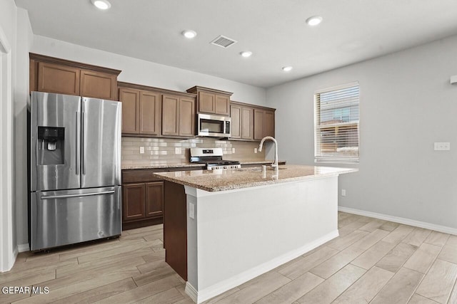 kitchen with sink, light stone counters, tasteful backsplash, a center island with sink, and stainless steel appliances