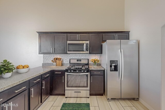 kitchen with appliances with stainless steel finishes, light stone counters, dark brown cabinets, light tile patterned floors, and decorative backsplash