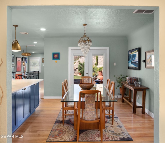 dining space with light hardwood / wood-style floors, a textured ceiling, french doors, and an inviting chandelier