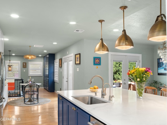 kitchen featuring light hardwood / wood-style flooring, blue cabinetry, hanging light fixtures, and sink