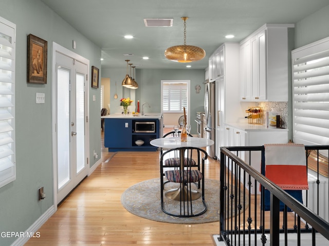 kitchen featuring appliances with stainless steel finishes, white cabinetry, backsplash, hanging light fixtures, and light wood-type flooring