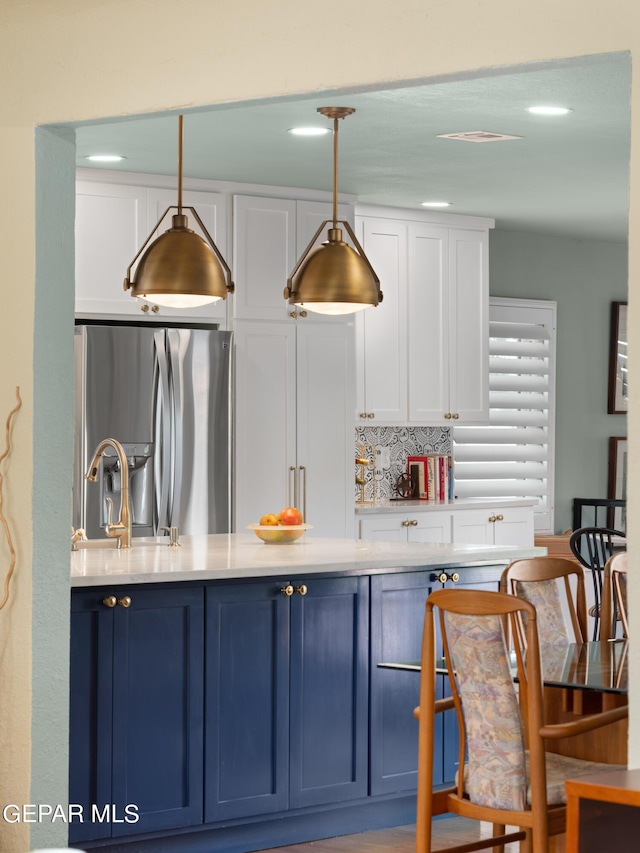 kitchen with decorative backsplash, hanging light fixtures, blue cabinetry, white cabinets, and stainless steel fridge