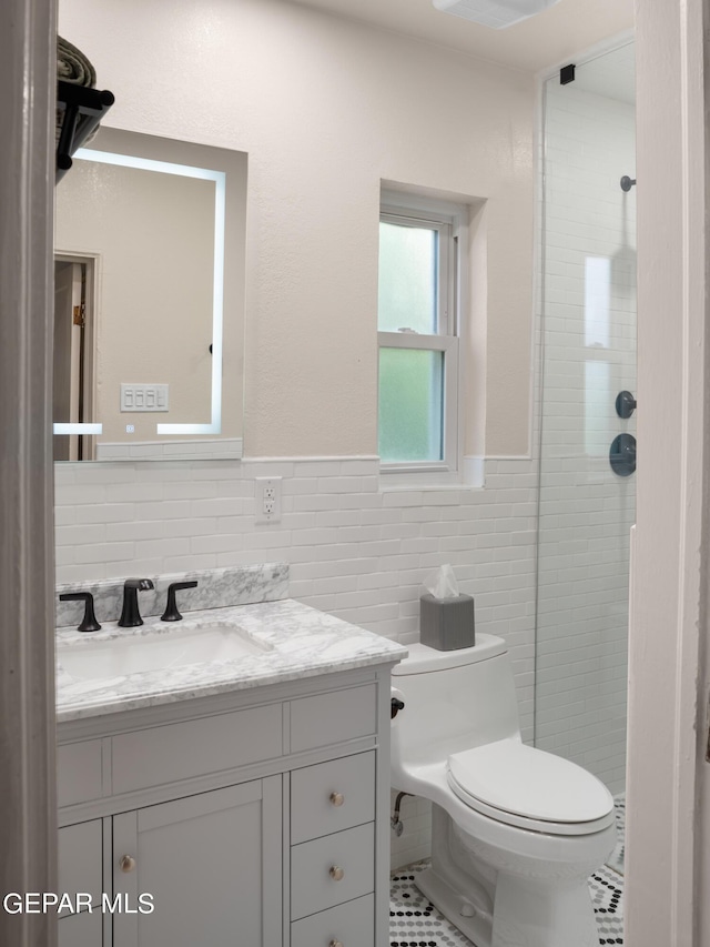 bathroom featuring toilet, a tile shower, tile patterned flooring, tile walls, and vanity