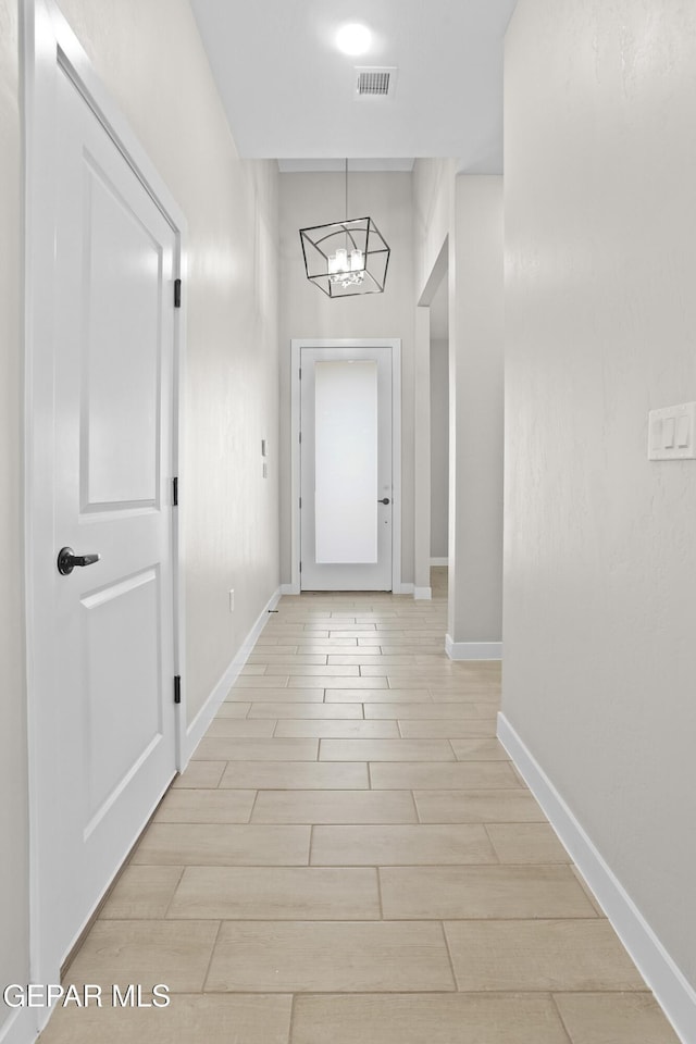 doorway to outside with baseboards, a notable chandelier, light wood-style flooring, and visible vents