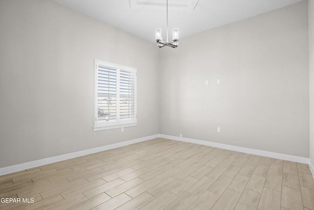 empty room featuring baseboards, an inviting chandelier, and light wood finished floors
