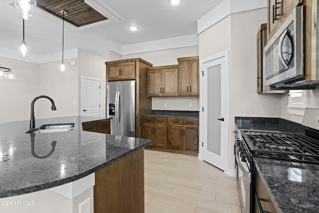 kitchen with light hardwood / wood-style floors, sink, appliances with stainless steel finishes, dark stone counters, and hanging light fixtures