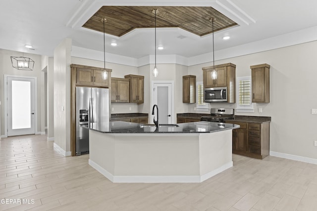 kitchen featuring a kitchen island with sink, pendant lighting, brown cabinets, a sink, and stainless steel appliances