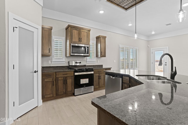 kitchen with stainless steel appliances, light hardwood / wood-style floors, sink, dark stone countertops, and pendant lighting