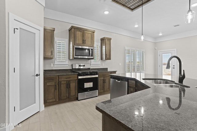 kitchen with a sink, pendant lighting, dark stone counters, and stainless steel appliances